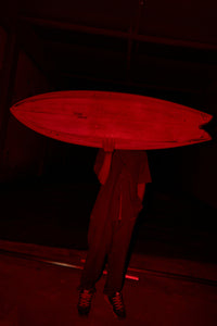 Person holding a surfboard in a dark setting with red lighting