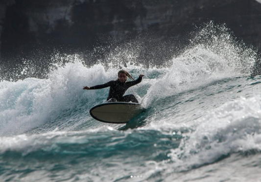 Tito doing a big carve with lots of spray  on a mini egg surfboard.